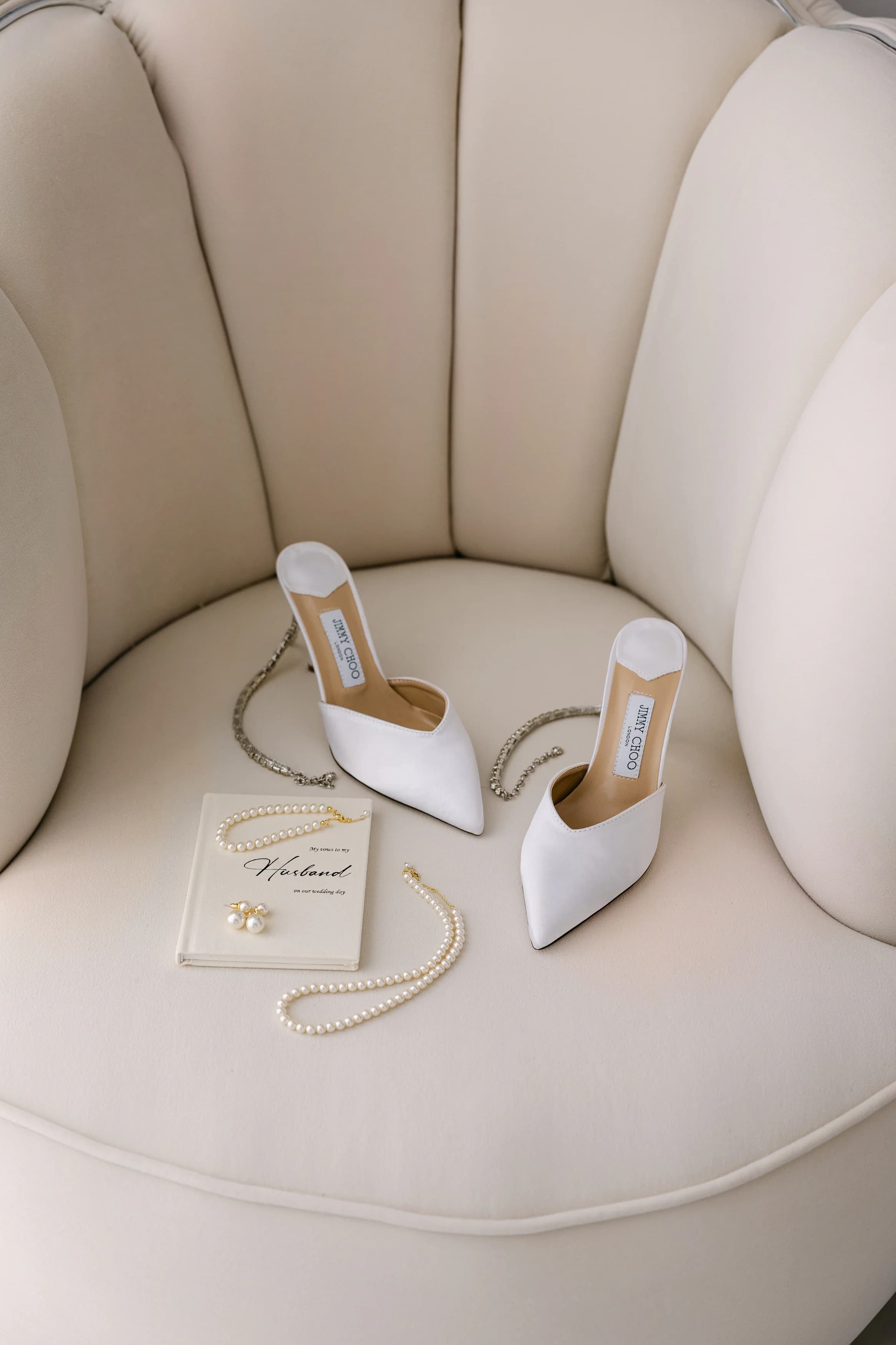 Bridal styling details at OZEA — white pointed-toe heels, pearl necklace and personalised journal on an ivory chair