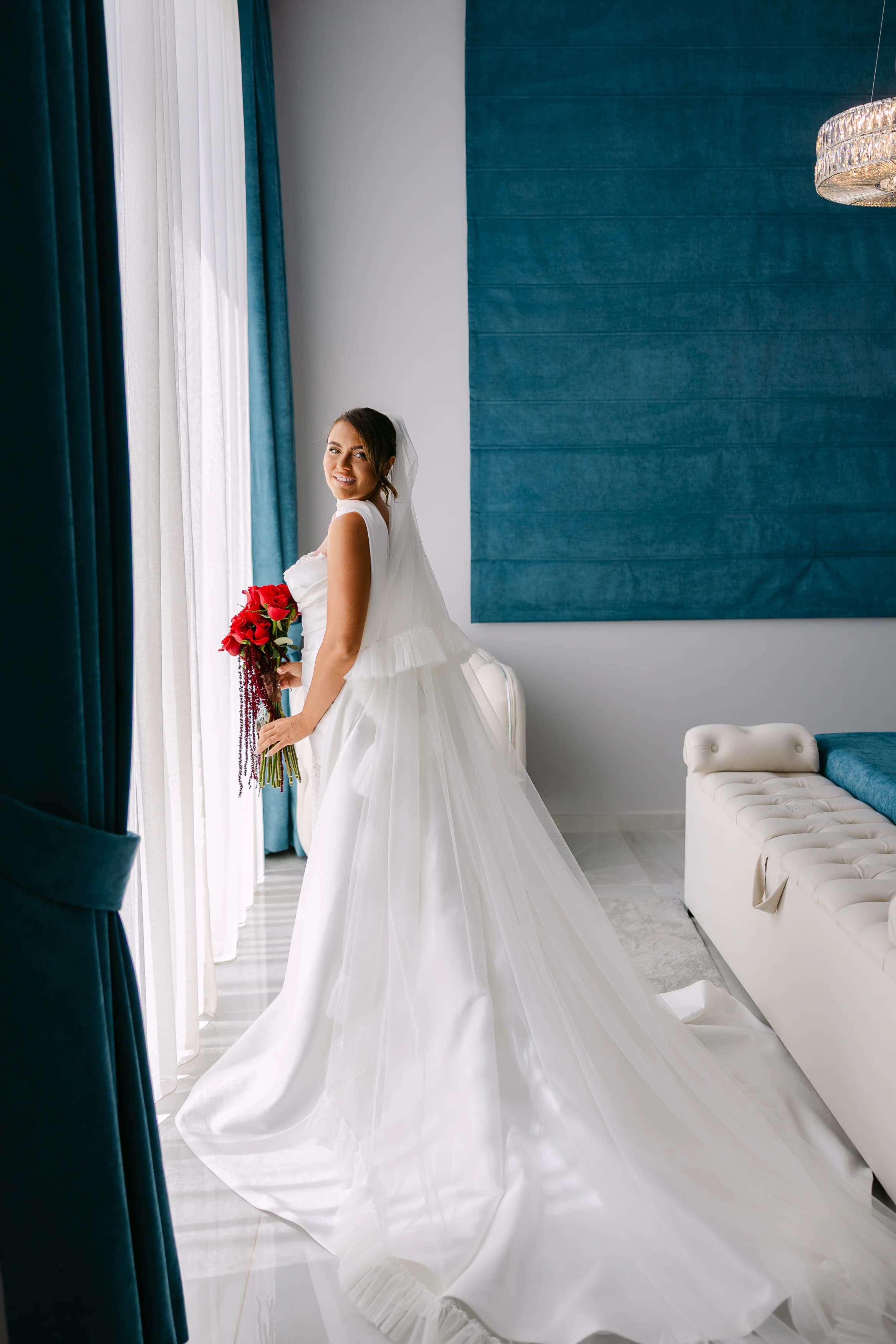 Bride in flowing white gown holding a red rose bouquet inside the OZEA bridal suite, Sea Caves Paphos
