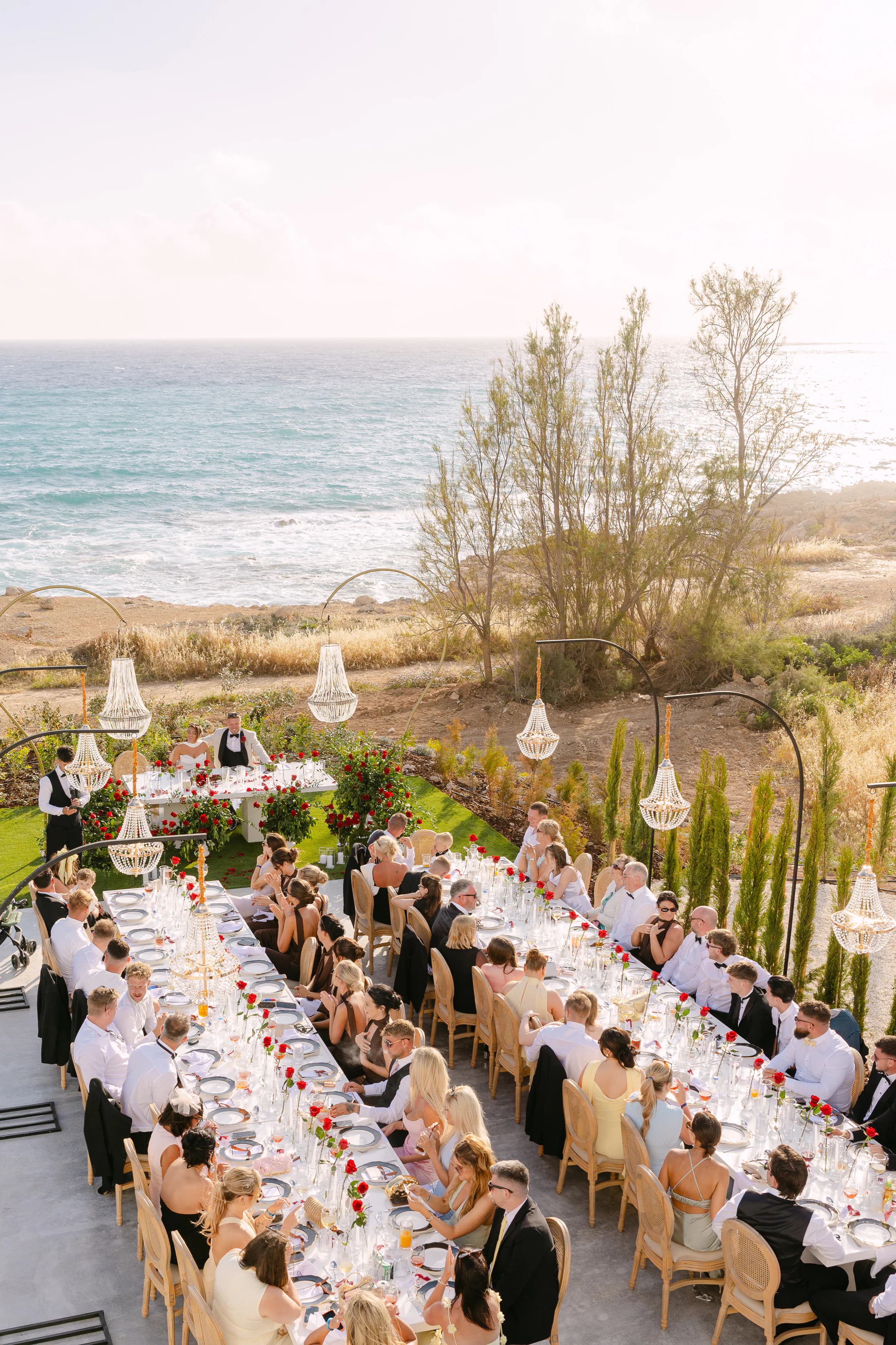 Golden-hour wedding reception at OZEA on the Sea Caves coast, Paphos — long banquet table planned and styled by Marry Me Cyprus