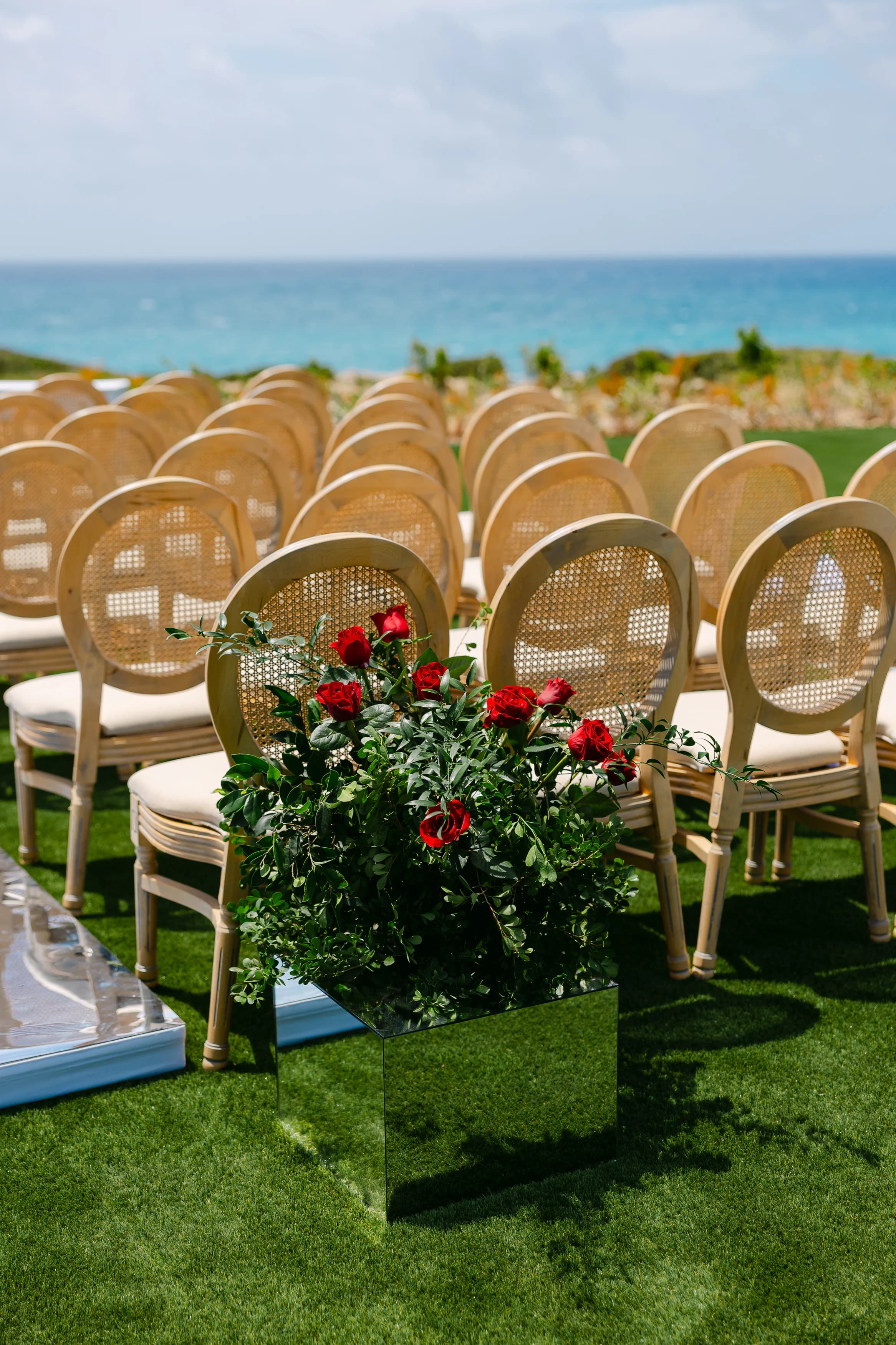 Cane Louis-style ceremony chairs in rows at OZEA with red rose aisle marker and the sea on the horizon, Sea Caves Paphos